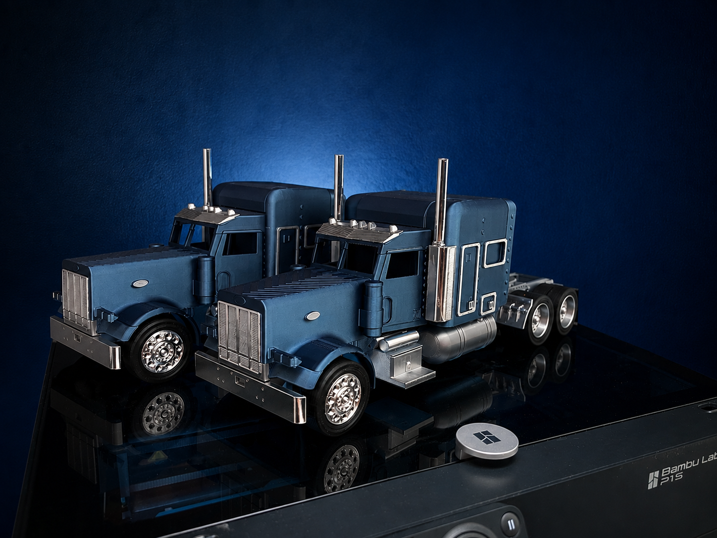 Two finished blue semi truck models displayed with dramatic lighting