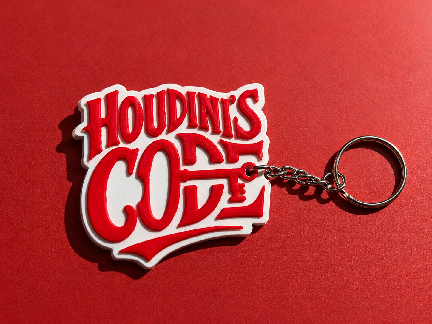 A red and white Houdini's Code keychain on a matching red background.